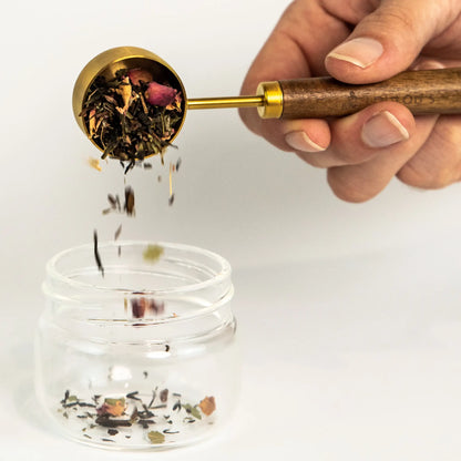 PuriTea scoop pouring organic loose leaf tea herbs and rose petals into glass infuser